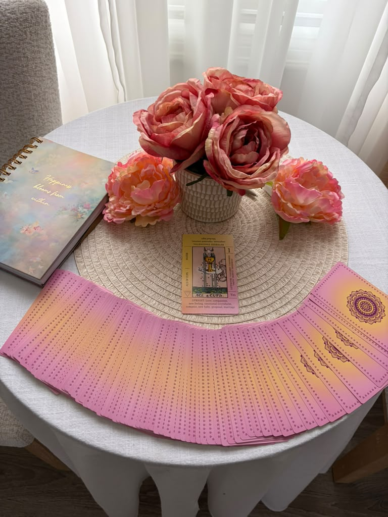 Kate Lovemore's tarot deck spread on a table with pink roses and a journal
