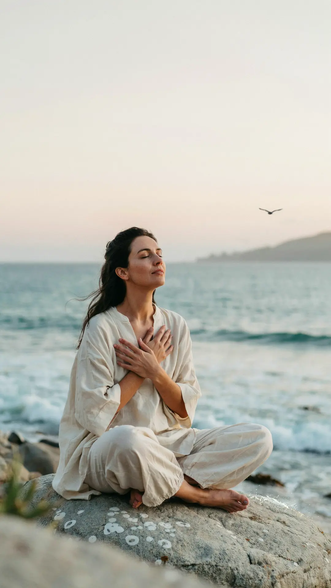 Woman meditating by the ocean at sunset with hands resting on her heart, representing chakra healing with Lorraine.